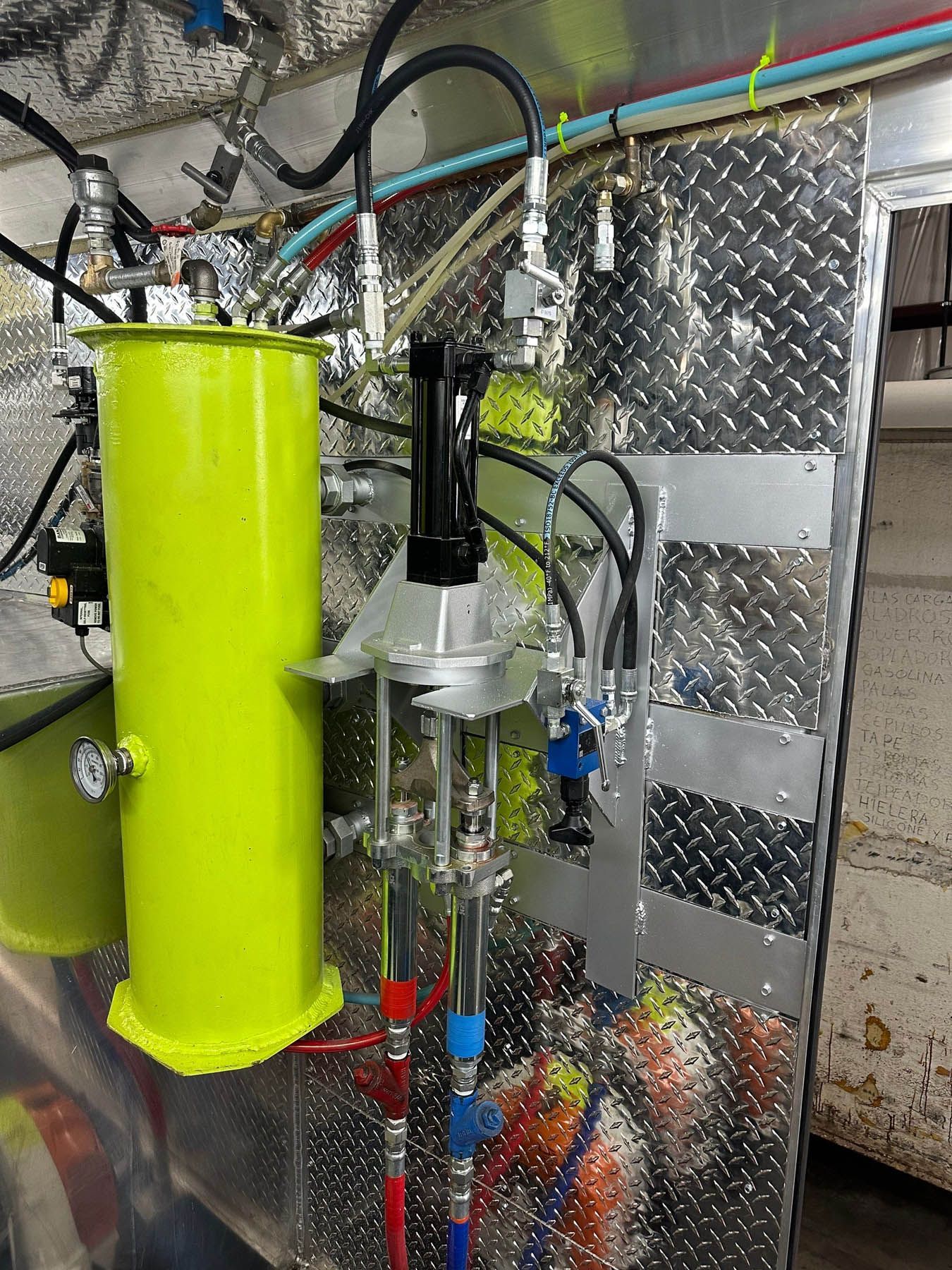 Yellow tank with black apparatus and colored hoses attached to a metal wall.