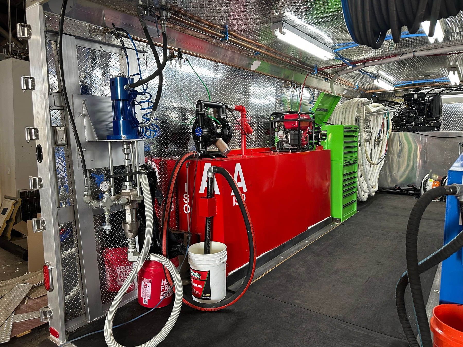 Interior view of a trailer equipped for fluid extraction. Red tank, tools, and machinery fill the space.