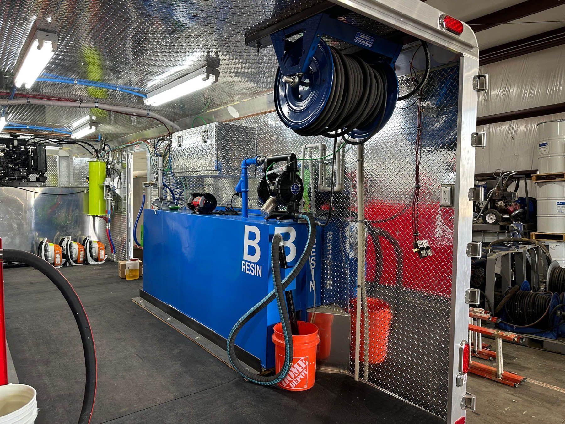 Interior of a utility trailer with cleaning equipment, including a blue tank and hose reel.