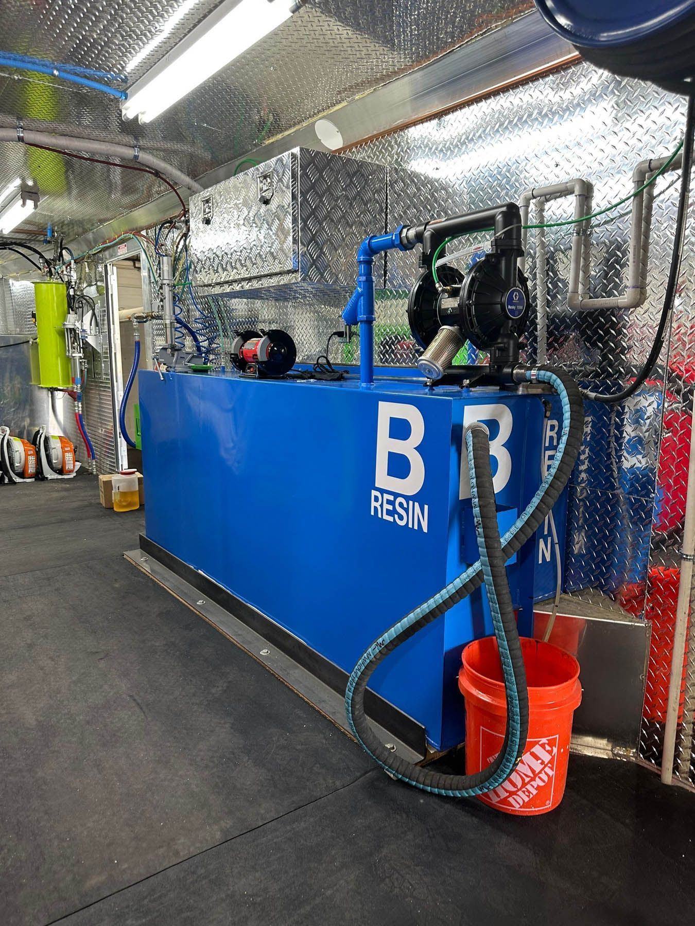 Blue resin tank inside a truck, with hoses, pumps, and a bucket. 
