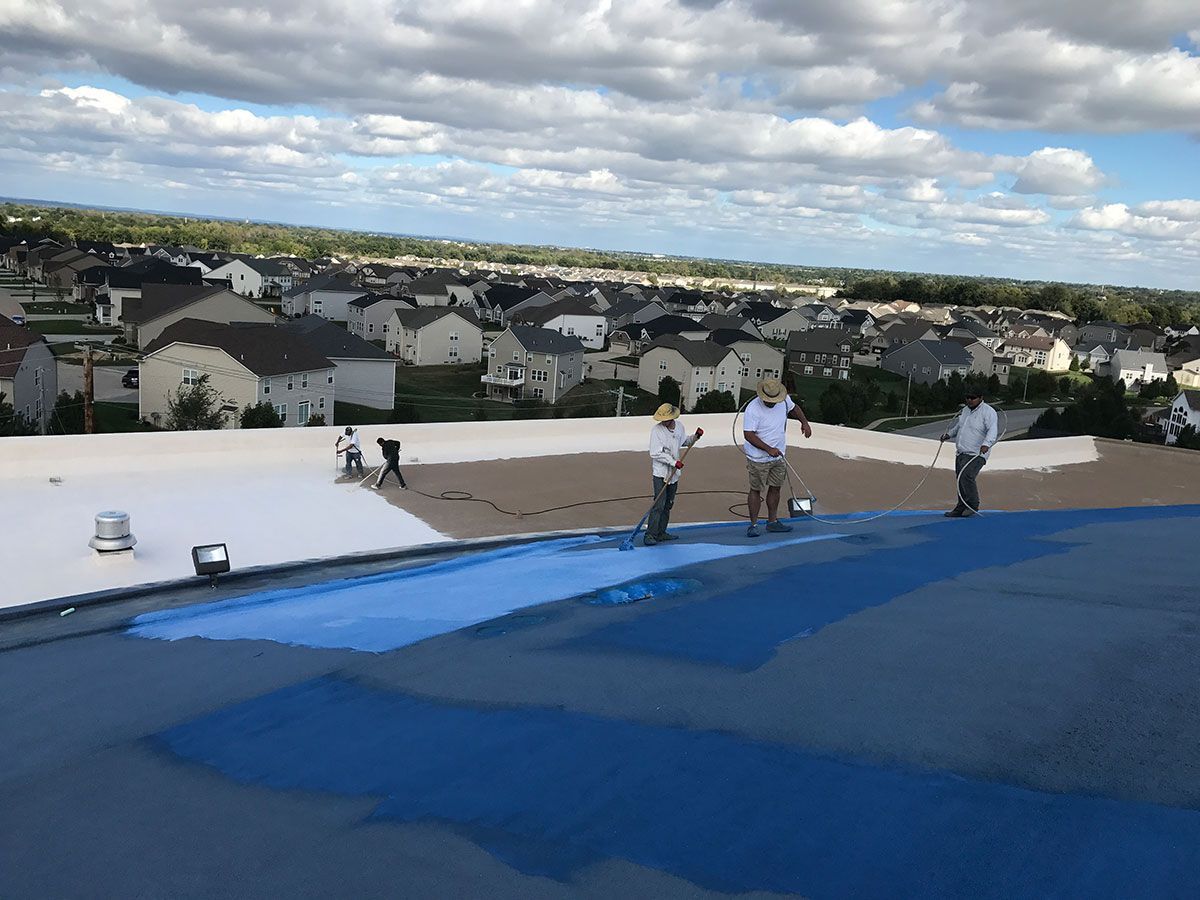 Roofers applying blue coating on a flat roof, residential neighborhood in background.