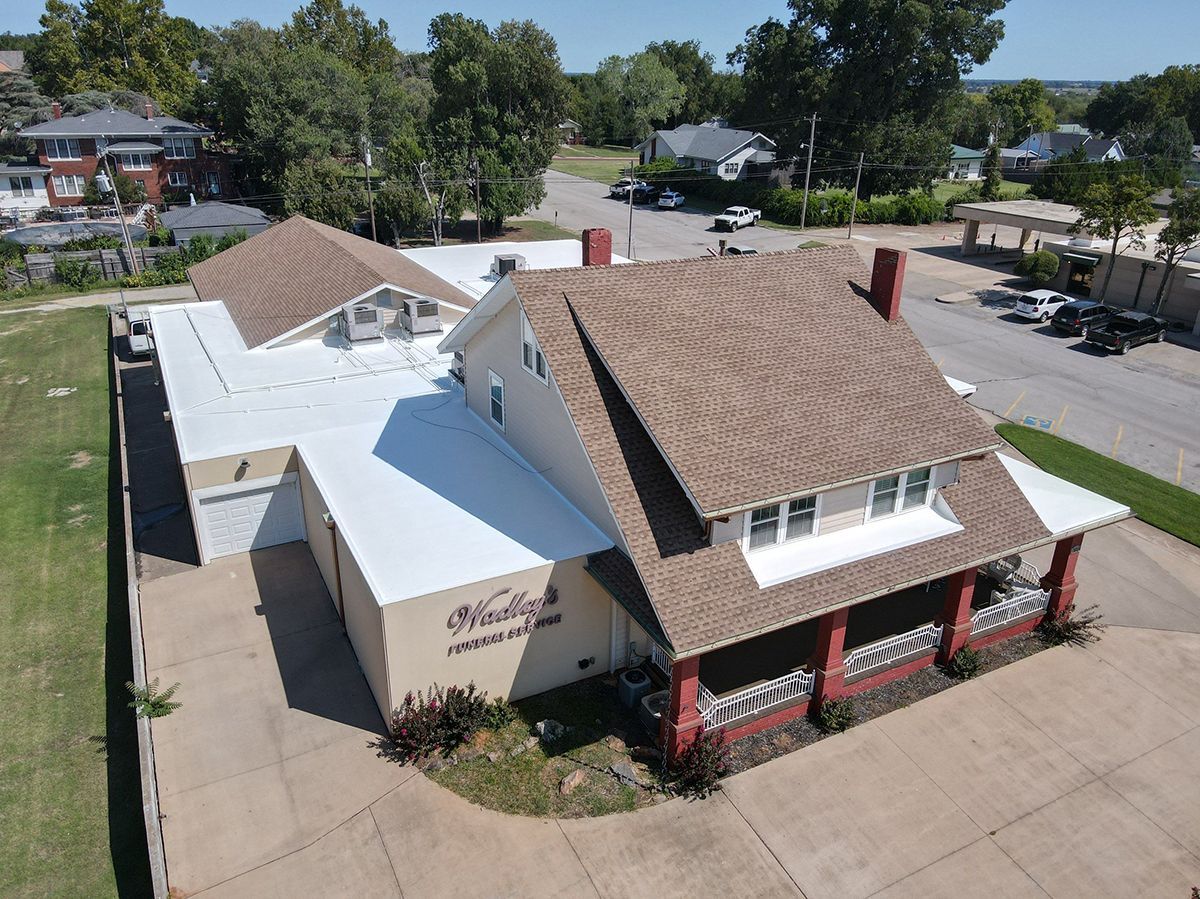 Aerial view of a tan and brown building with a flat white roof. Building has a porch and is near a road.