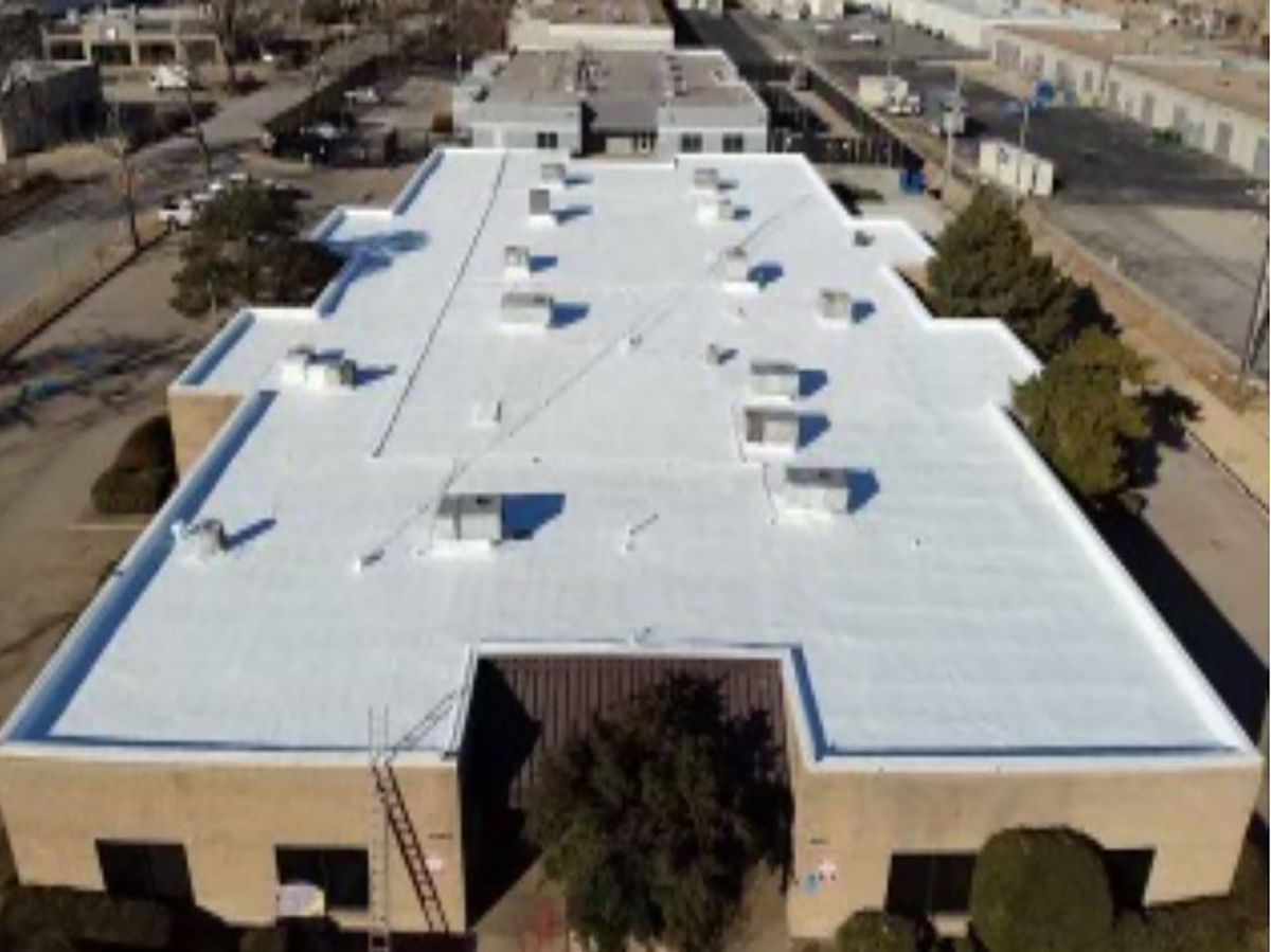 Aerial view of a tan commercial building with a white flat roof, multiple vents, and a surrounding cityscape.