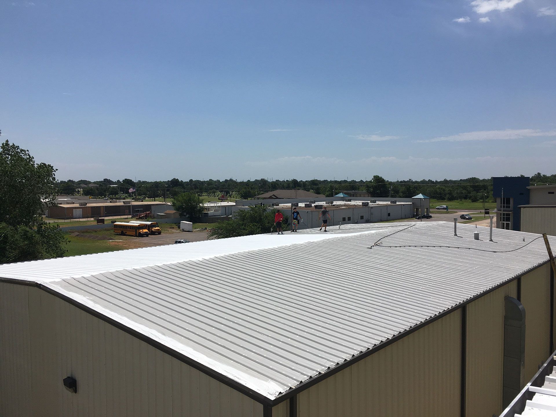 View of a corrugated metal roof on a building. Sunny day, clear blue sky; background with buildings and trees.