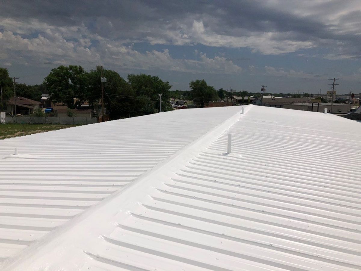 White roof with ridges, extending into the distance, under a cloudy sky, trees in the background.