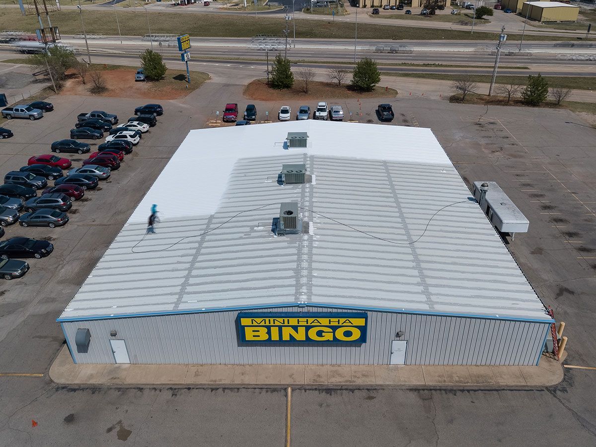 Bingo hall with a large, white metal roof and a parking lot full of cars.