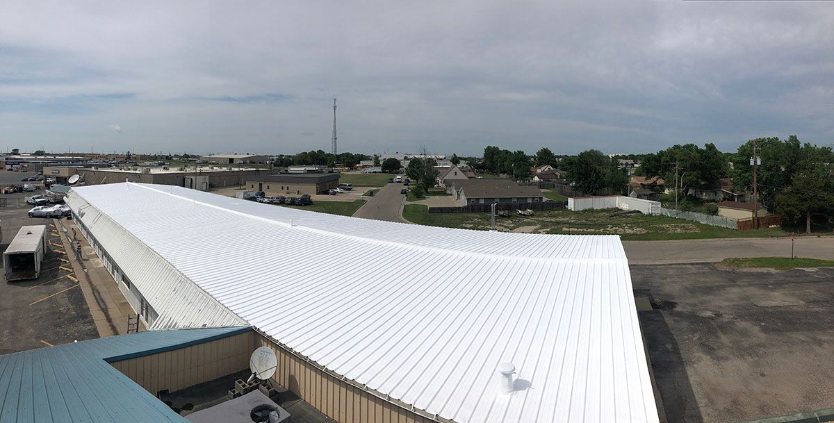 Overhead view of a large white corrugated metal roof of a commercial building, small town in background, overcast sky.