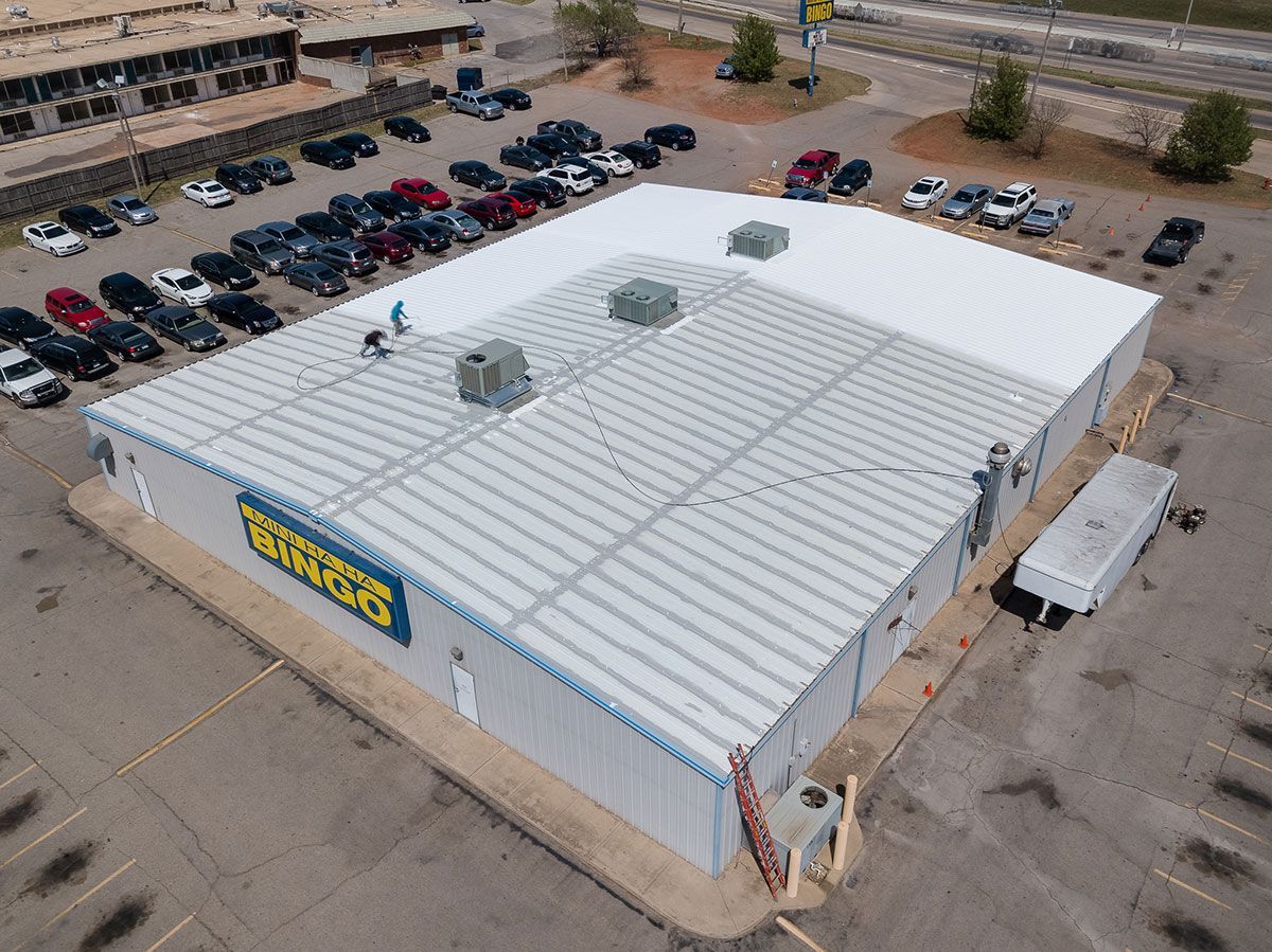 Aerial view of a large commercial building with a silver corrugated metal roof, surrounded by a parking lot.