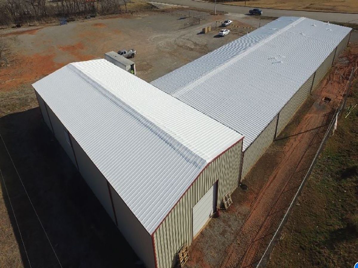 Aerial view of a large industrial building with a silver metal roof and brown siding.