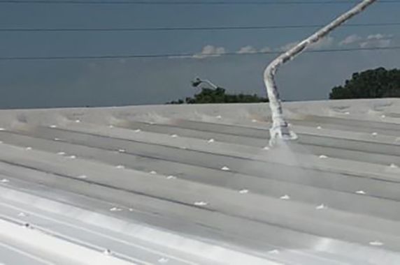 Spraying white coating on a metal roof.