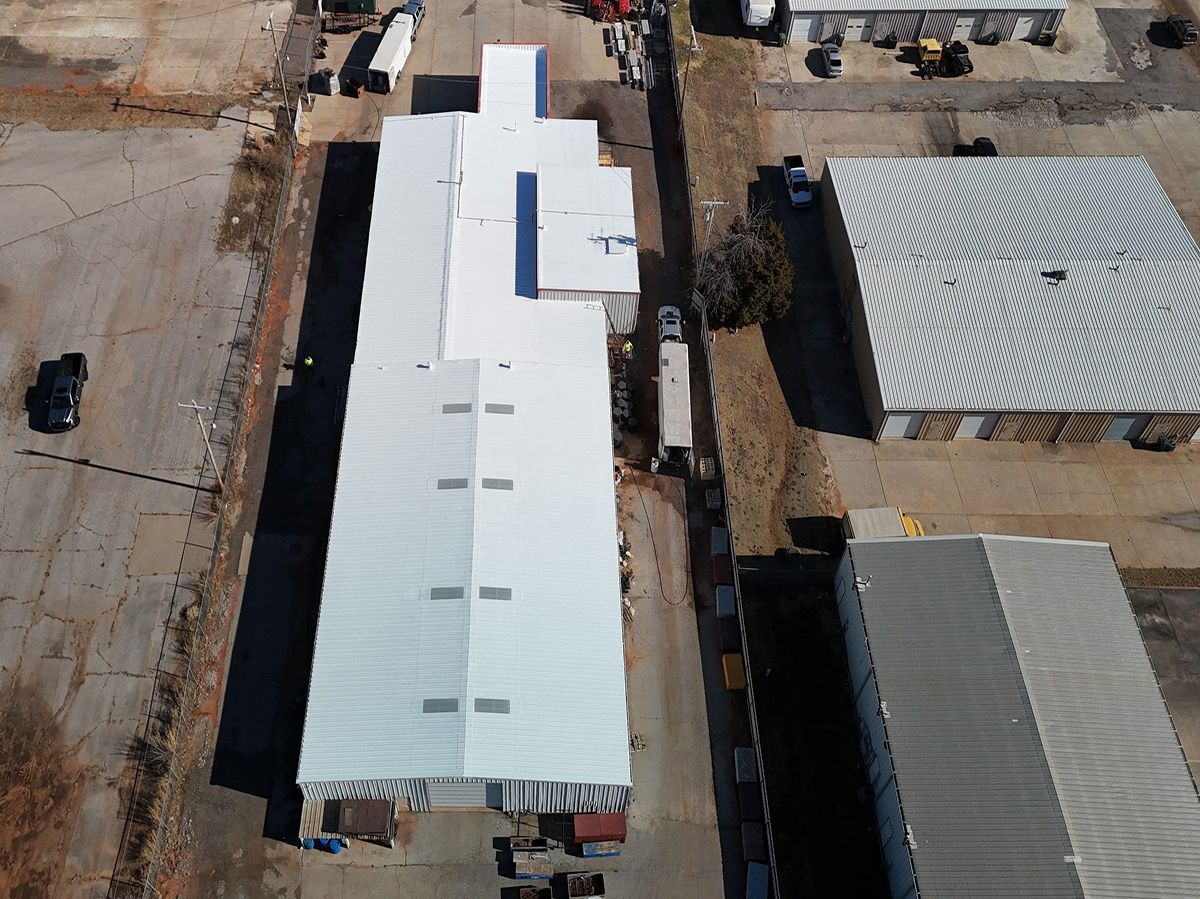 Aerial view of industrial buildings with light-colored roofs, set on a paved lot.