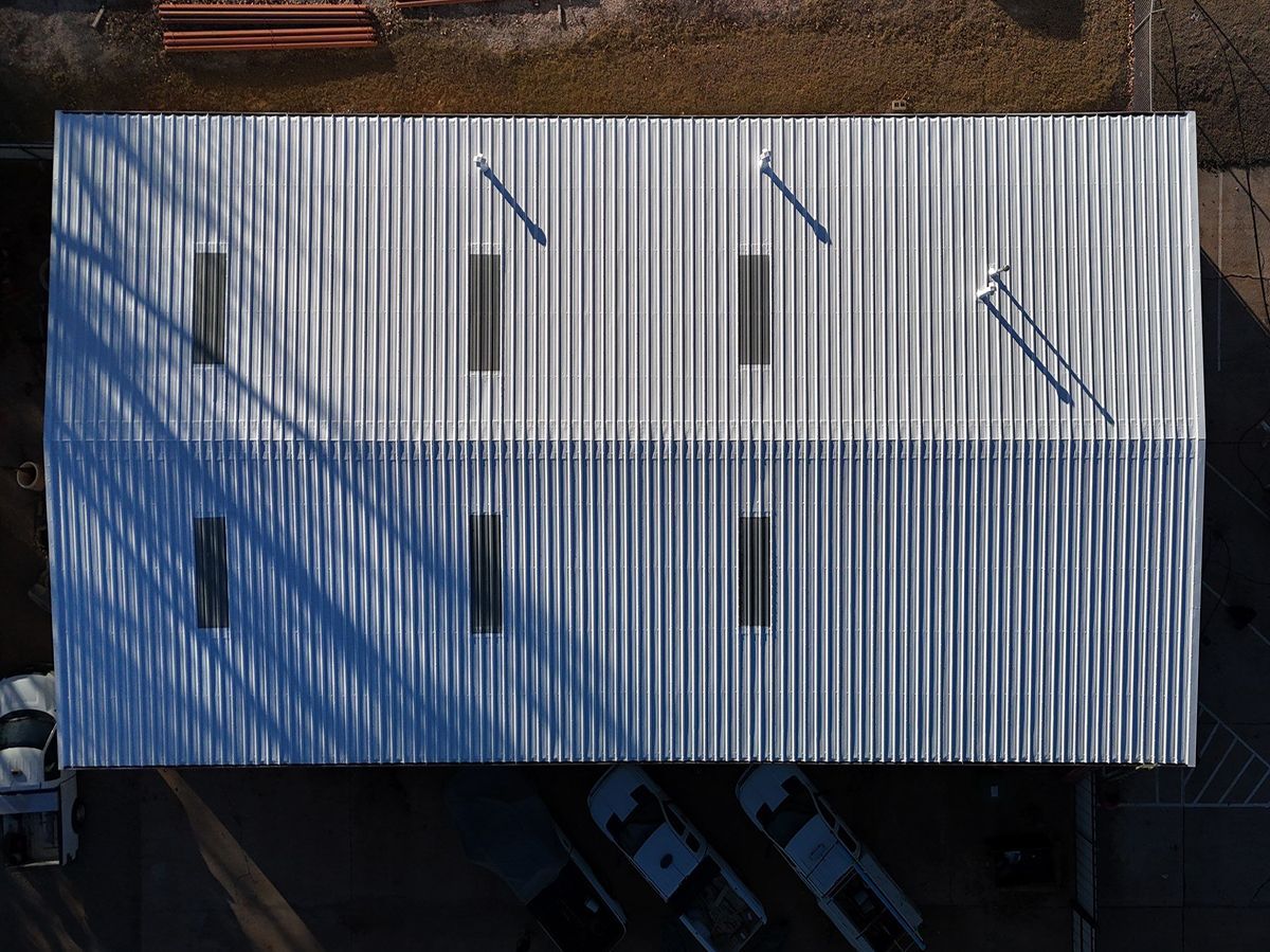 Overhead view of a building with a corrugated metal roof, shadows, and parked vehicles below.