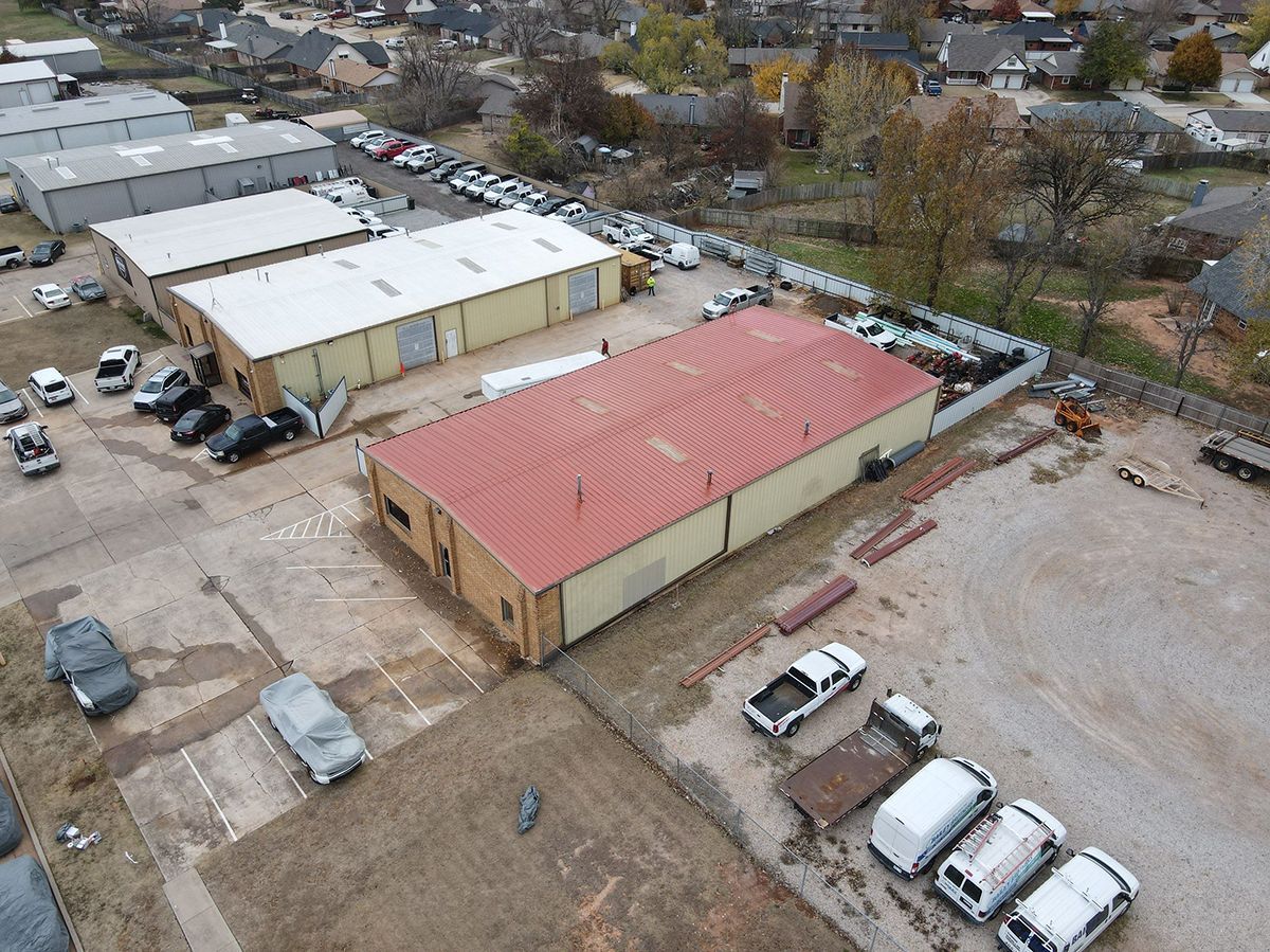 Aerial view of several industrial buildings and vehicles in an outdoor setting with residential houses in the background.