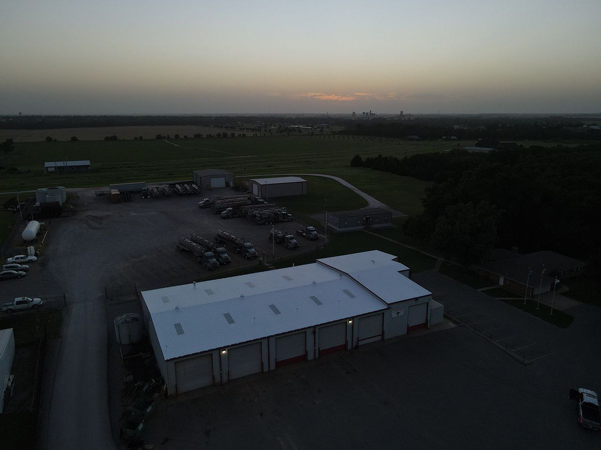 Aerial view of a commercial property at dusk. A large warehouse building with a silver roof dominates the foreground.