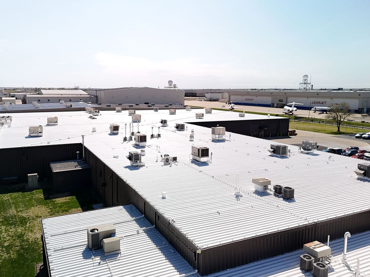 Aerial view of a flat commercial roof with many HVAC units and other equipment. Brown siding.