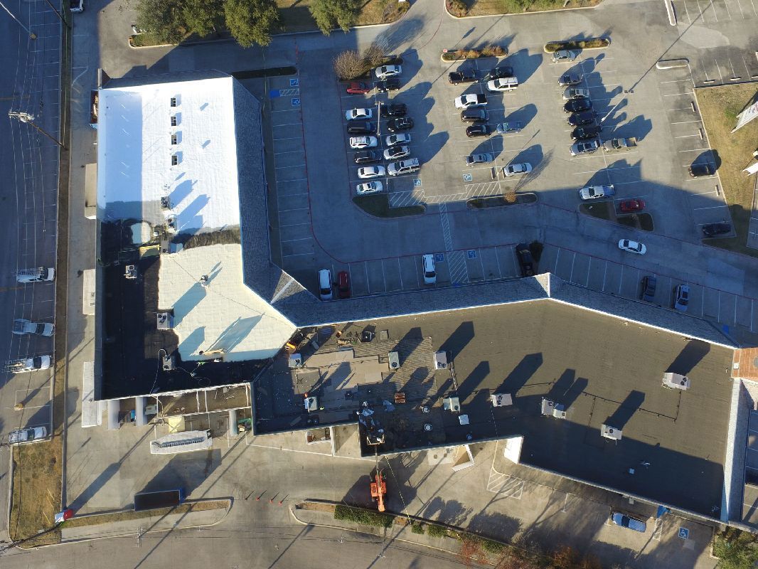 Aerial view of a building and parking lot with parked cars, shadows, and trees.