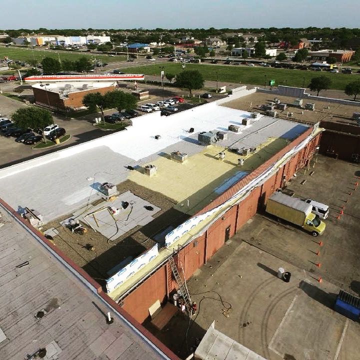 Aerial view of a commercial building roof under repair. White and tan roofing materials with trucks and equipment.