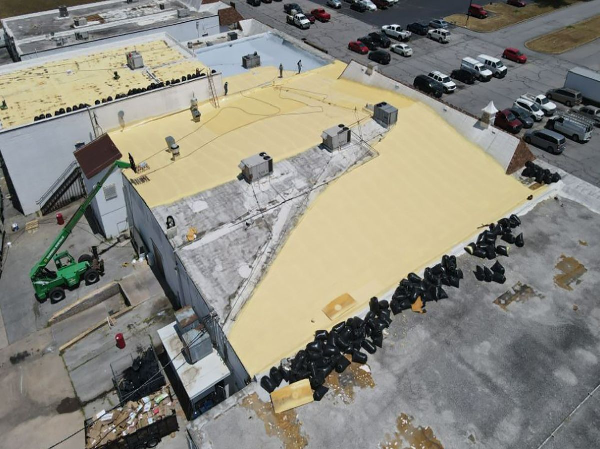 Aerial view of building with roof repair; yellow insulation, construction equipment, and black debris bags.