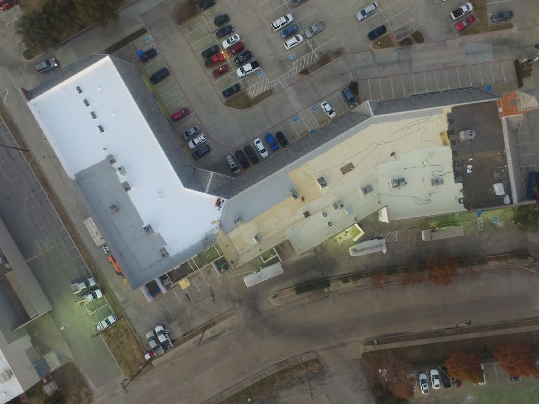 Aerial view of a commercial building with a parking lot. Cars parked around.