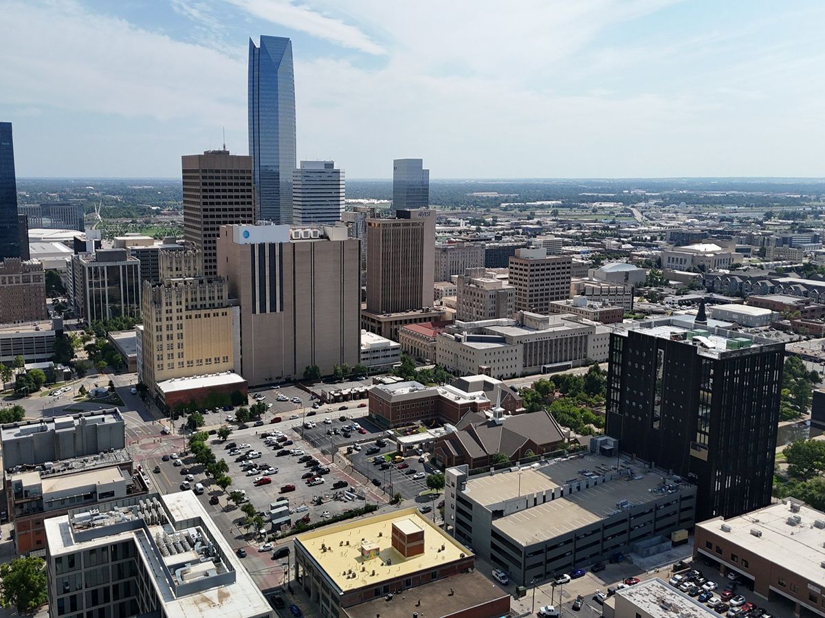 Aerial view of Oklahoma City skyline on a sunny day. Tall modern buildings are visible against a clear blue sky.