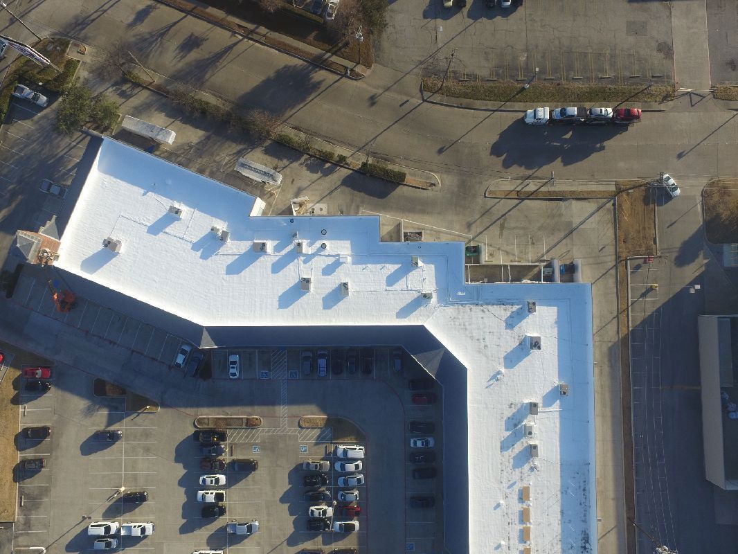 Aerial view of a building with a white roof, a parking lot, and cars.