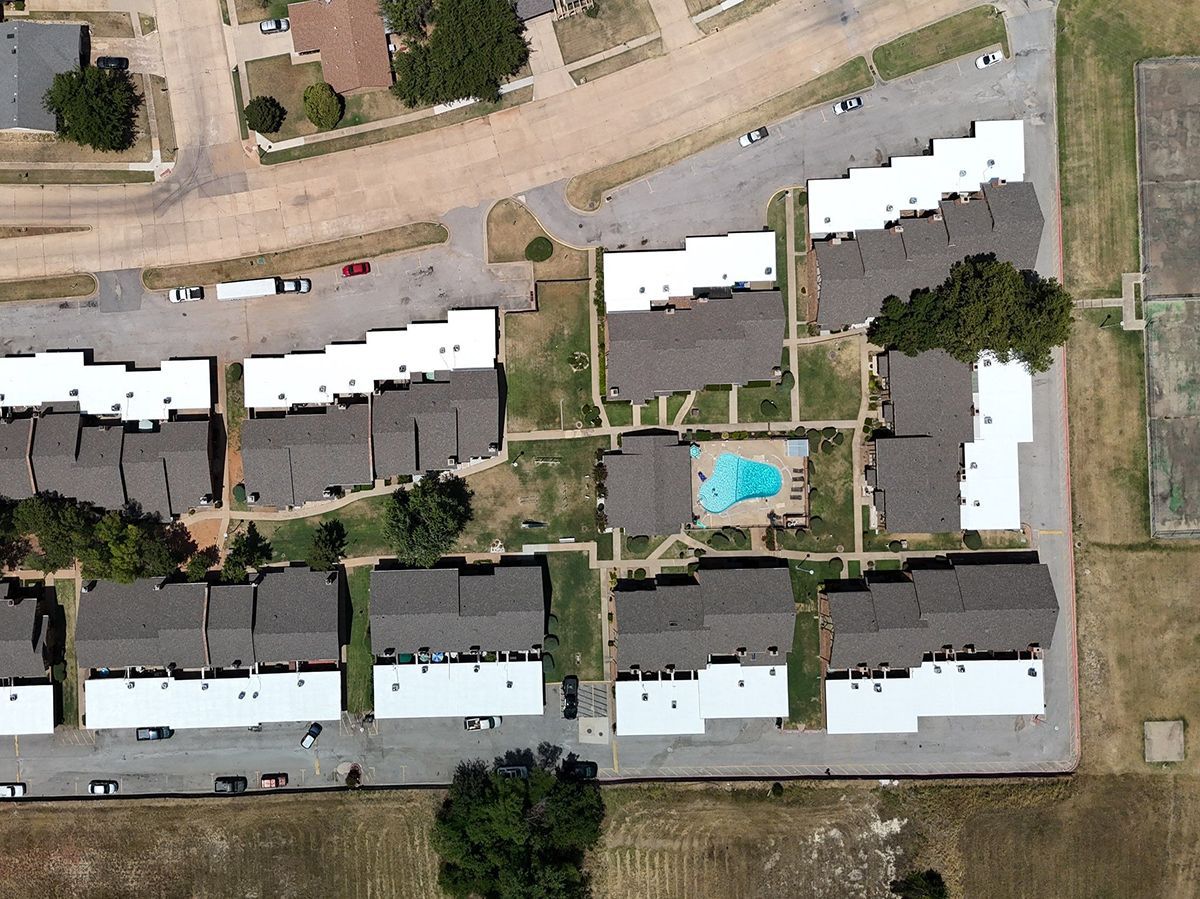 Aerial view of apartment complex with a pool, trees, and parking.