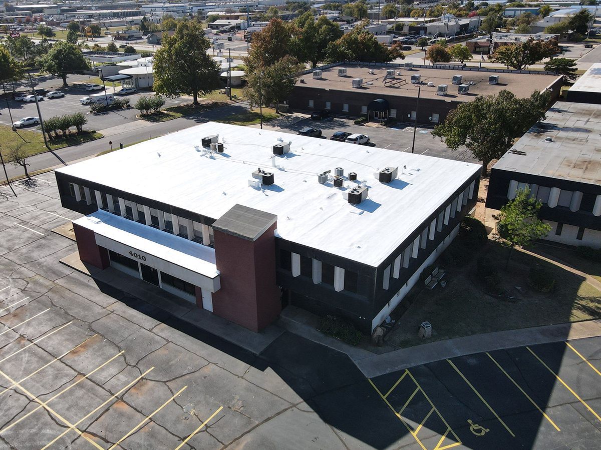 Aerial view of a commercial building with a flat roof and parking lot in an urban setting.