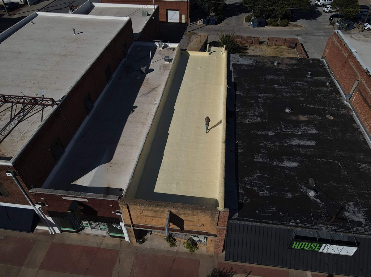 Aerial view of person walking on a long yellow-painted roof in a town with brick buildings.