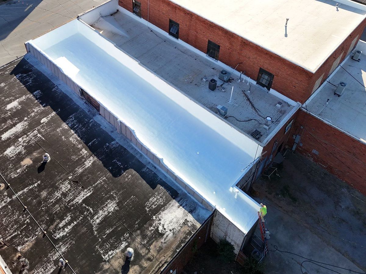 Aerial view of a building roof with a long, reflective, white coating reflecting sunlight.