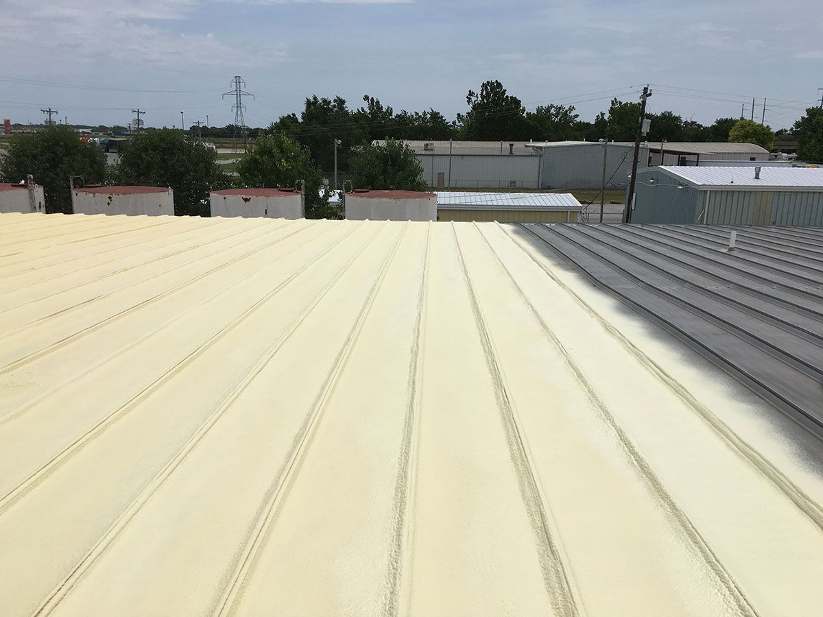 Yellow foam insulation applied to a corrugated metal roof, with a partially insulated gray section.