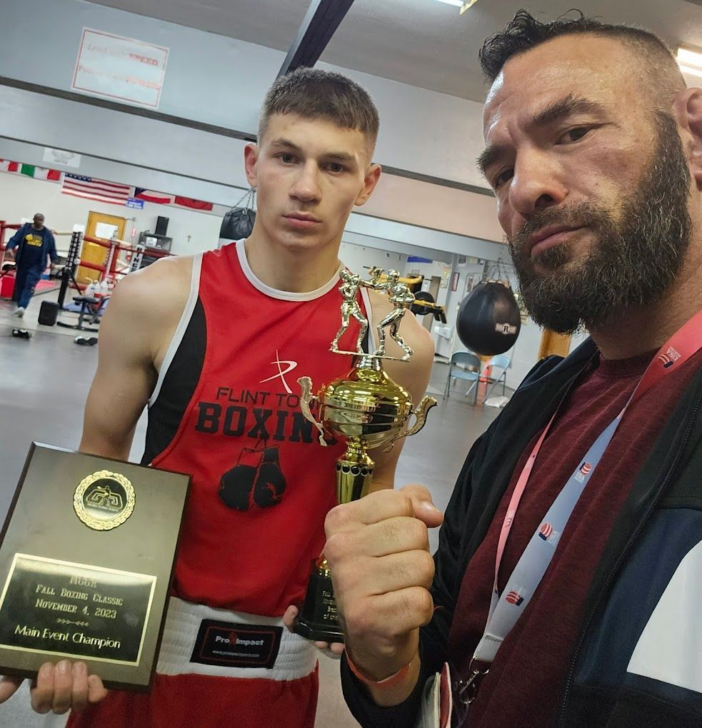 A man in a flint boxing shirt is holding a trophy