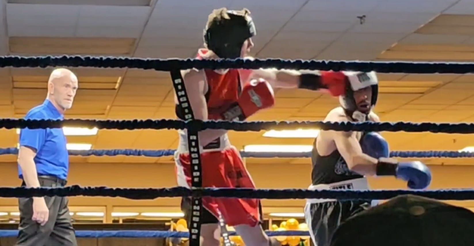 Two men are boxing in a ring with a referee watching
