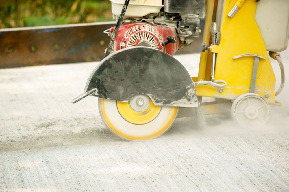 Yellow Concrete Saw Cutting Into a Concrete Surface, Creating Dust — Coastcut Concrete Cutting Pty Ltd in Maitland, NSW