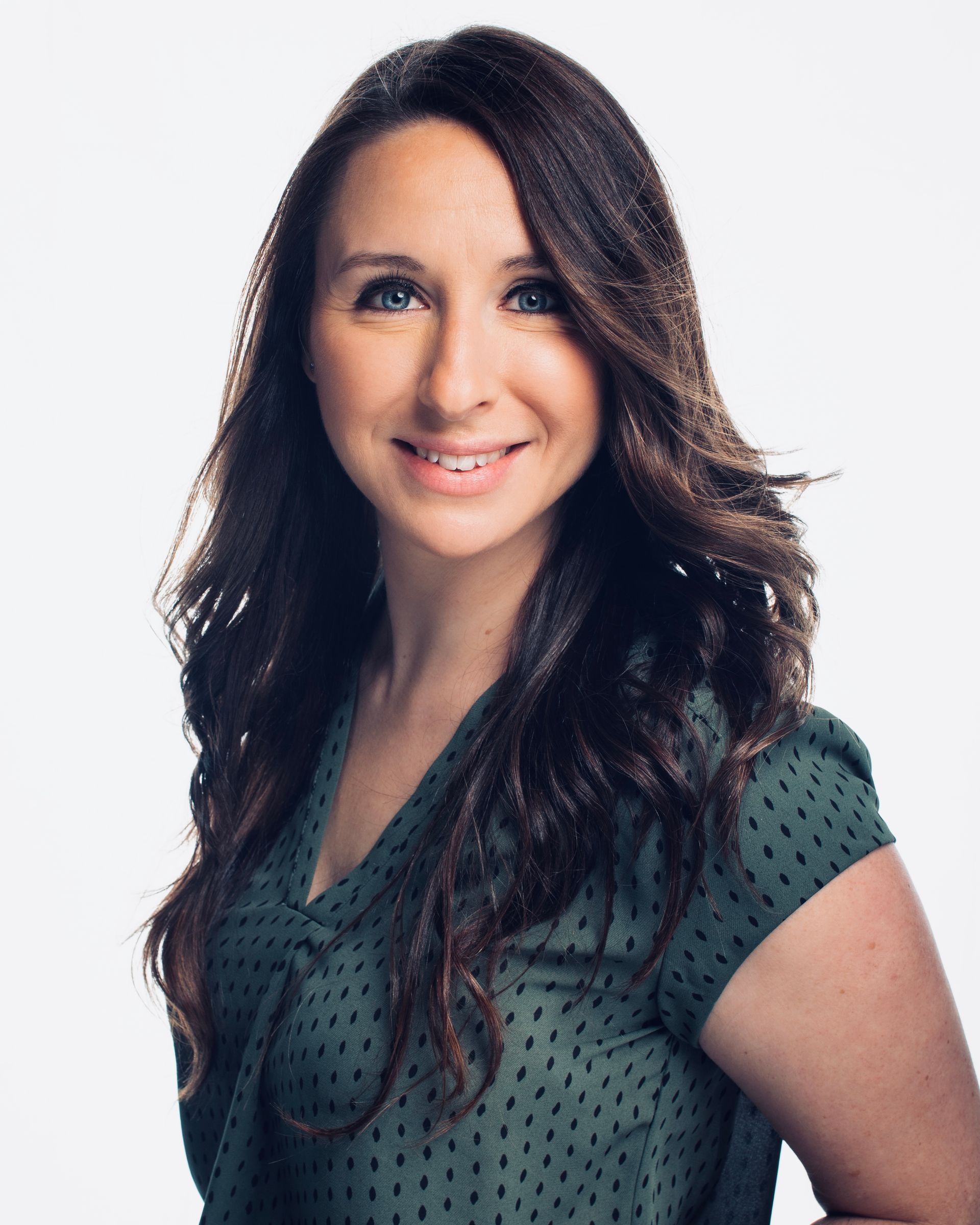 Woman with long brown hair, smiling in a green blouse against a white background.