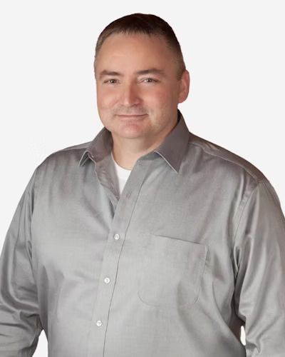 Man wearing a gray button-down shirt smiles, looking at the camera.