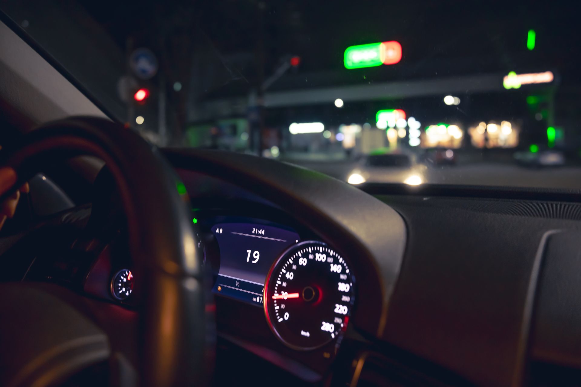 Dashboard view from a car driving at night; speedometer at 15 mph. In the background, a lit gas station.