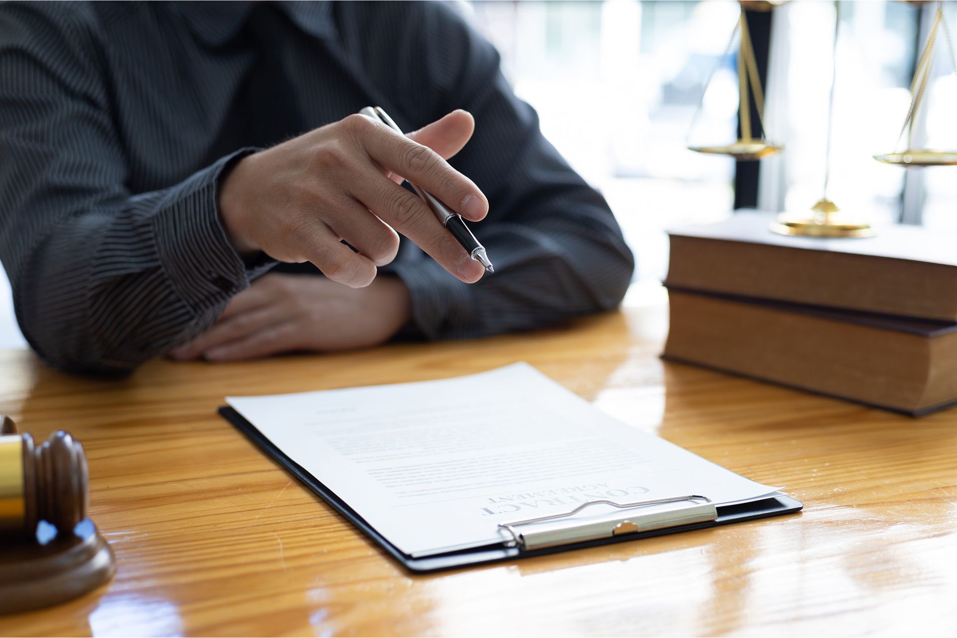 Person in suit points pen at a document on a desk. Scales of justice and books in the background.
