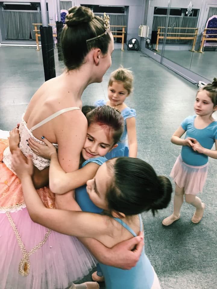 Group of women in dresses, posing for a photo in a studio; neutral backdrop, floral patterns, smiles.