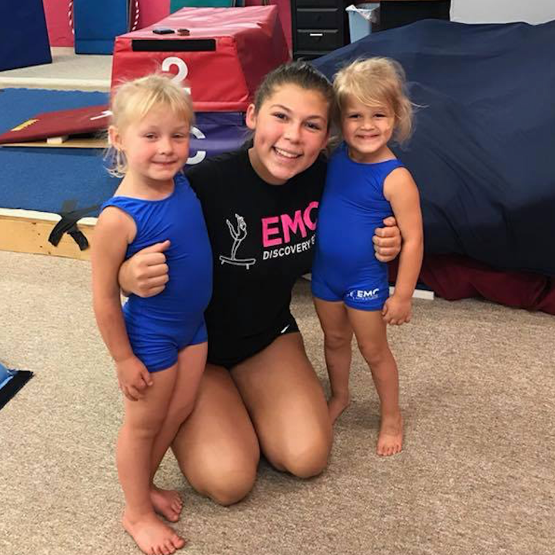 Two young female dancers smiling; one in black, the other in a sparkly costume.