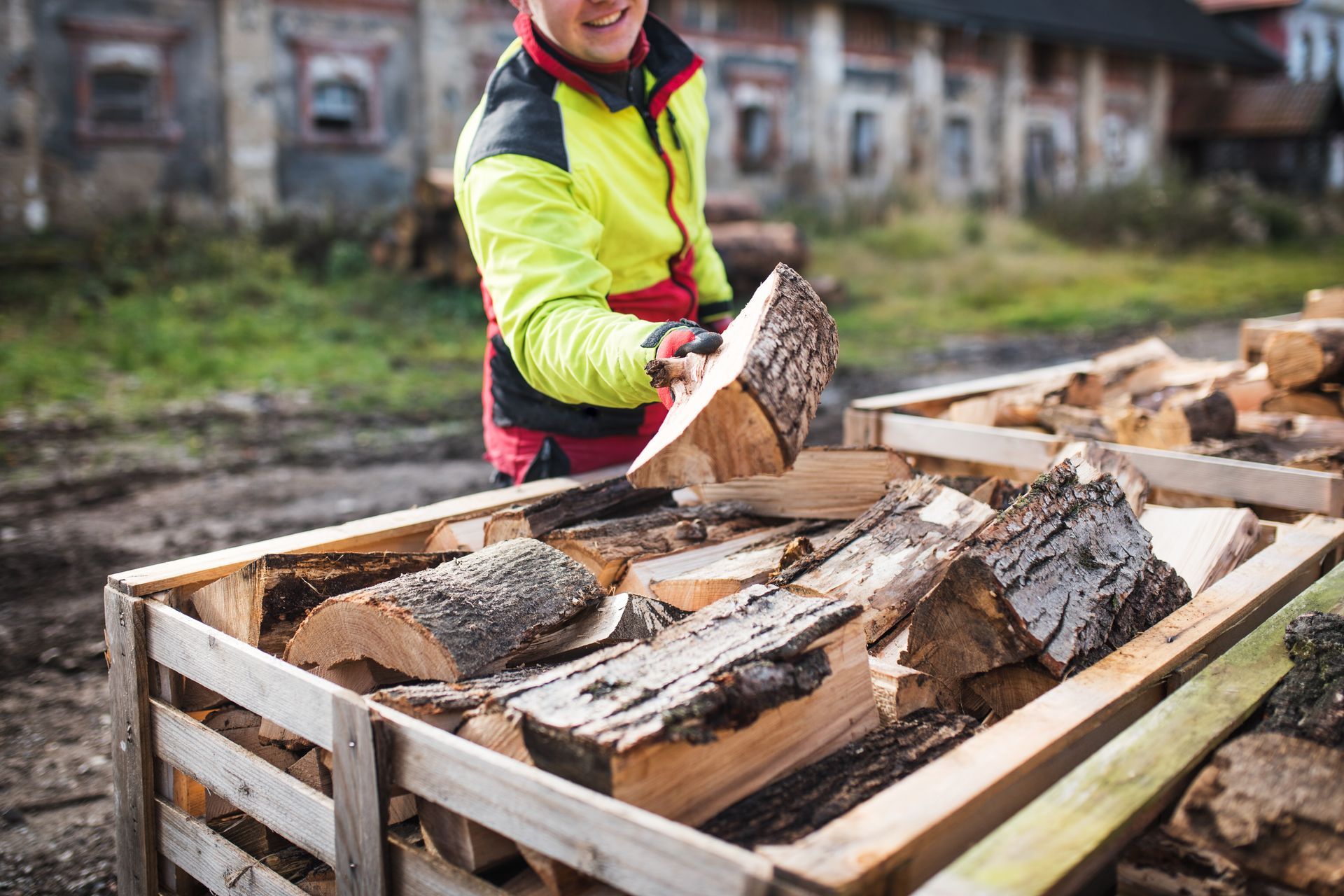 A man is standing next to a wooden crate filled with logs.