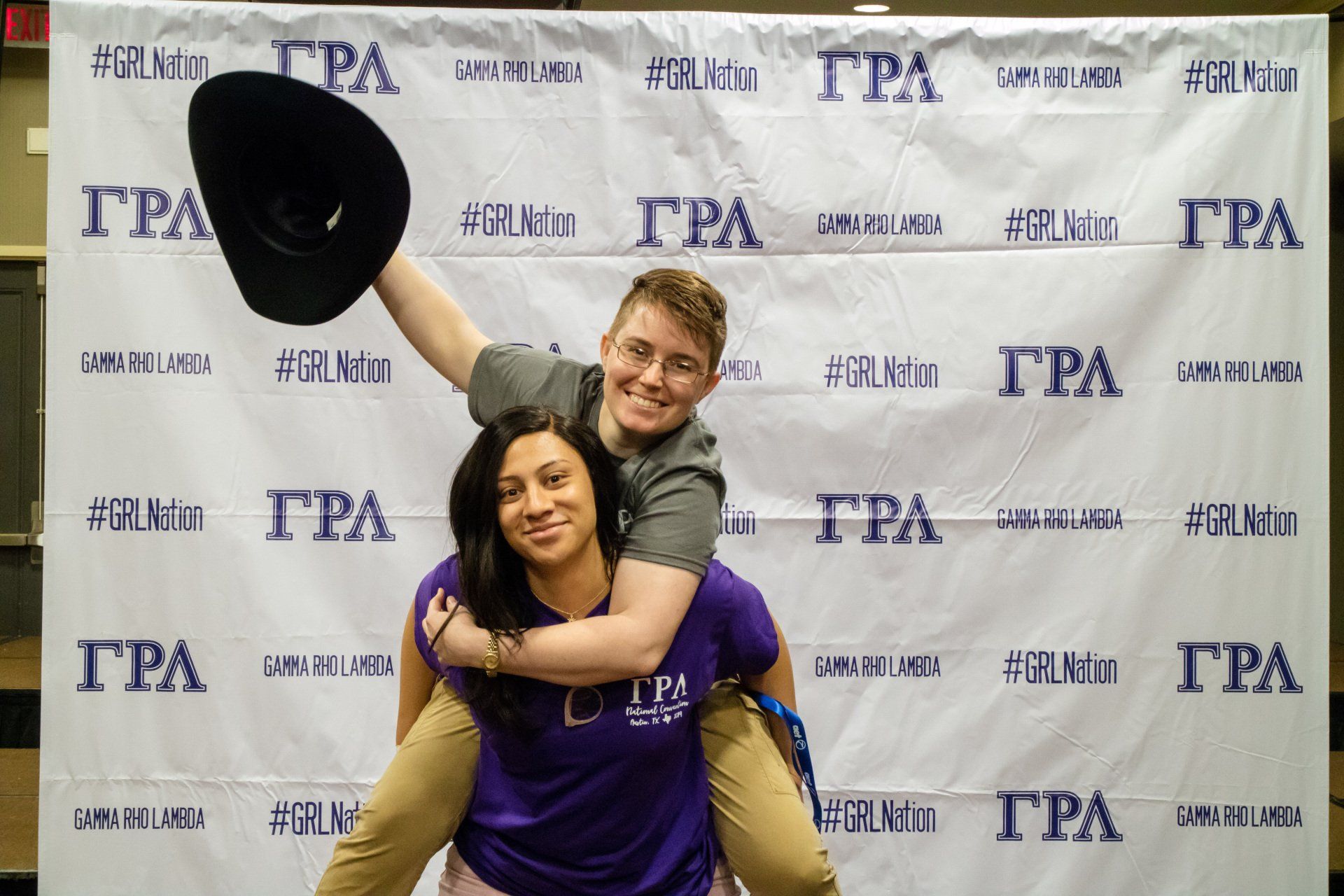 Two people pose together. One person is on the other's back and is holding out a cowboy hat