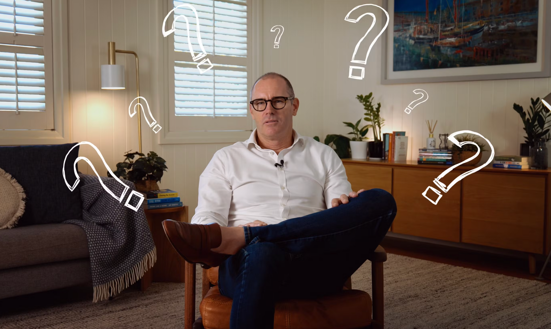 Byron sitting in a chair, surrounded by question marks, in a home interior.