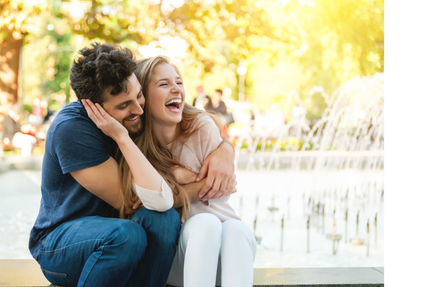 A man and a woman are sitting next to each other and laughing in front of a fountain.