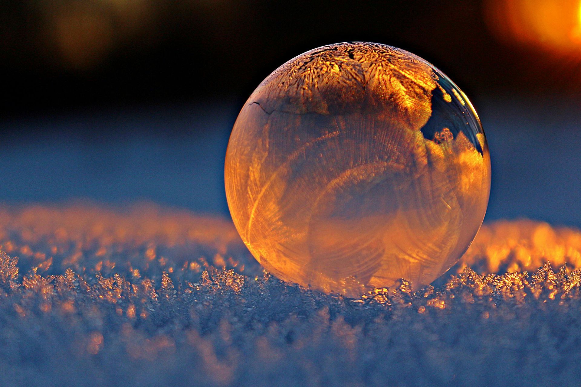Frozen soap bubble resting on snow, lit by golden sunlight.