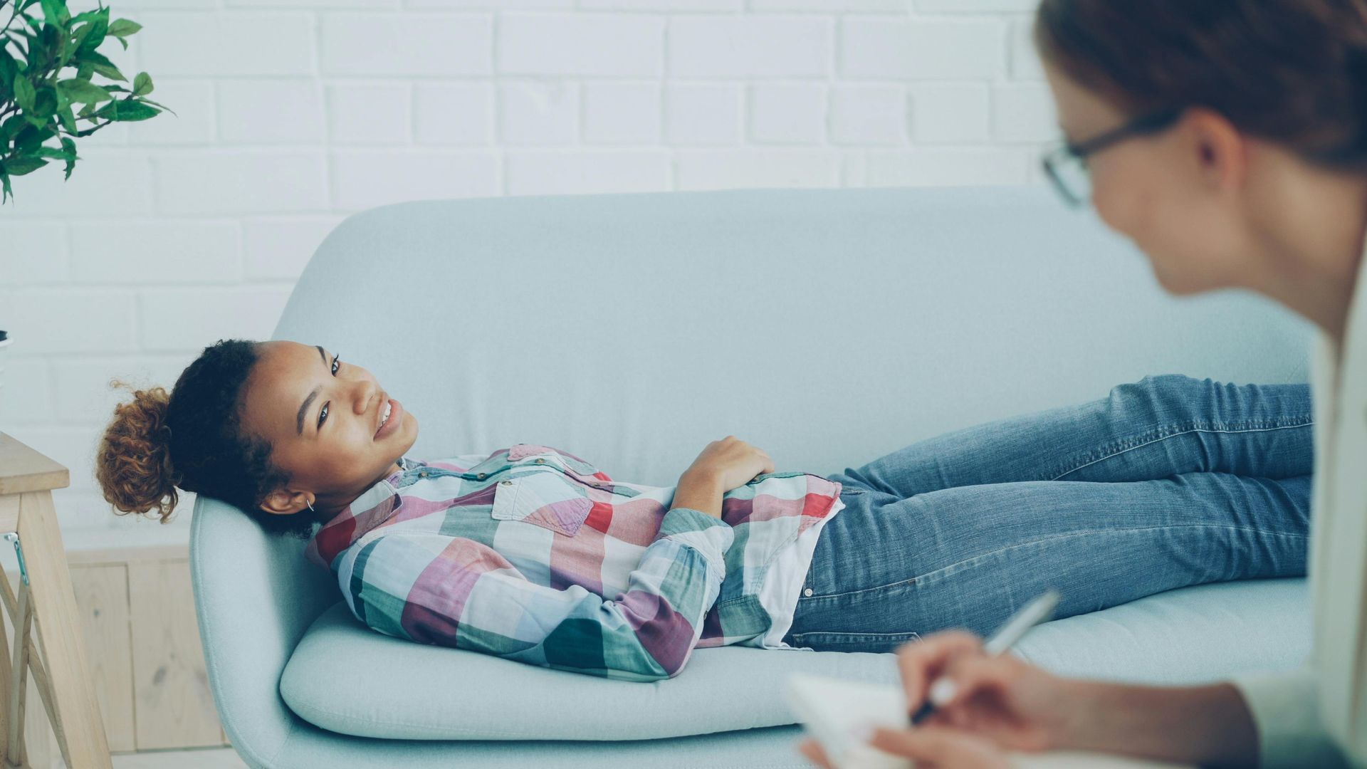 A patient lies on a couch while a therapist takes notes during a counseling session.