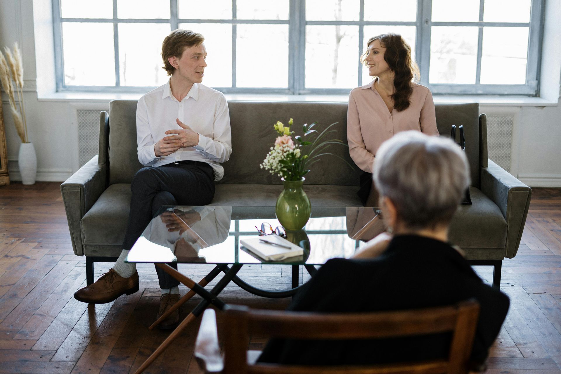 Couple on couch in therapy, talking to a seated therapist, interior.