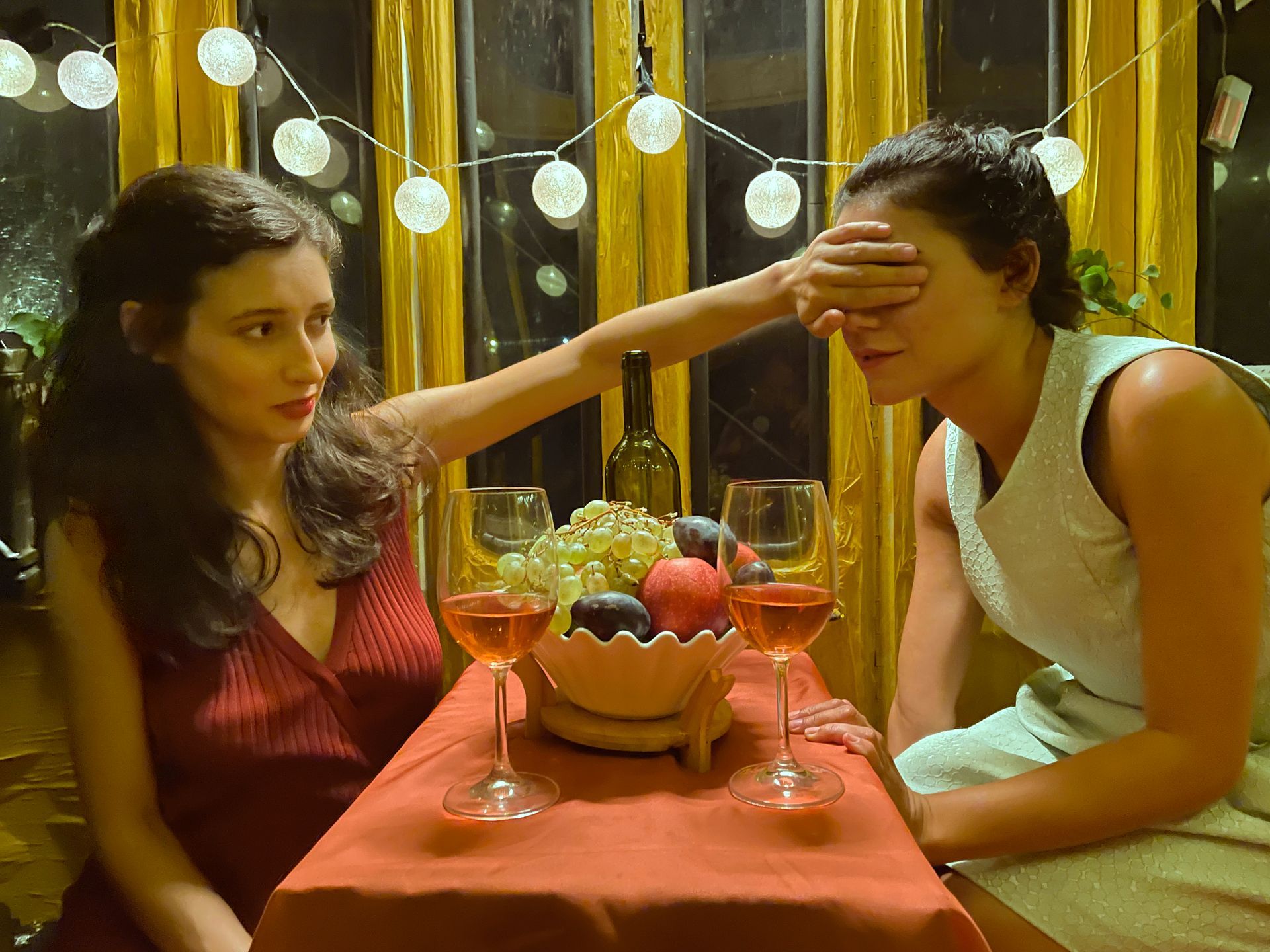 Zwei Frauen sitzen an einem Tisch mit Weingläsern und einer Schale Obst