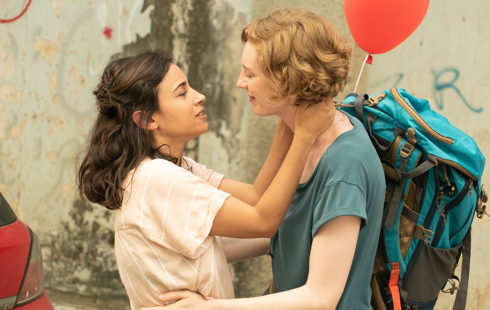 Eine Frau mit einem Rucksack umarmt eine andere Frau mit einem roten Ballon