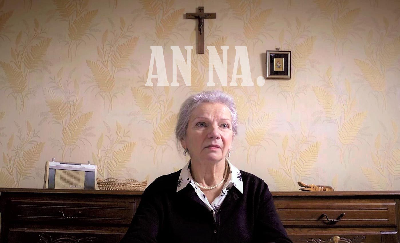 Eine ältere Frau sitzt vor einer Wand mit dem Wort Anna darauf