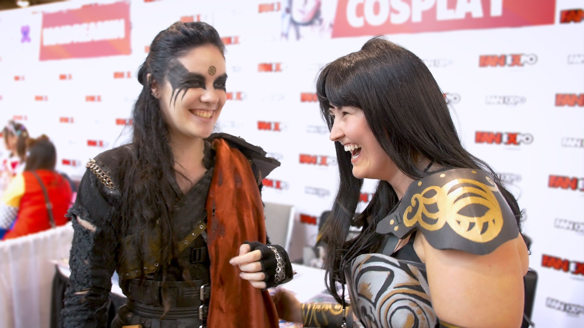 Zwei Cosplayerinnen lachen zusammen auf einer Convention. Eine ist als Lexa verkleidet, die andere als Xena.
